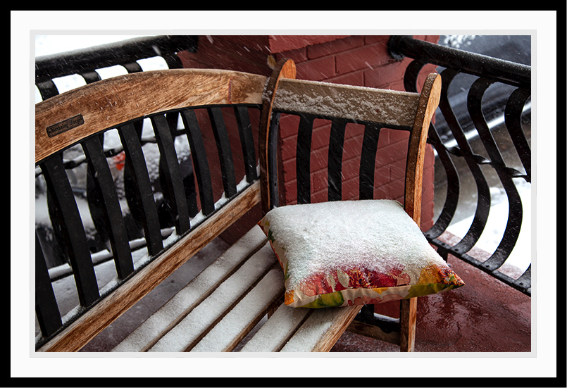 Bench in the snow with a pillow.